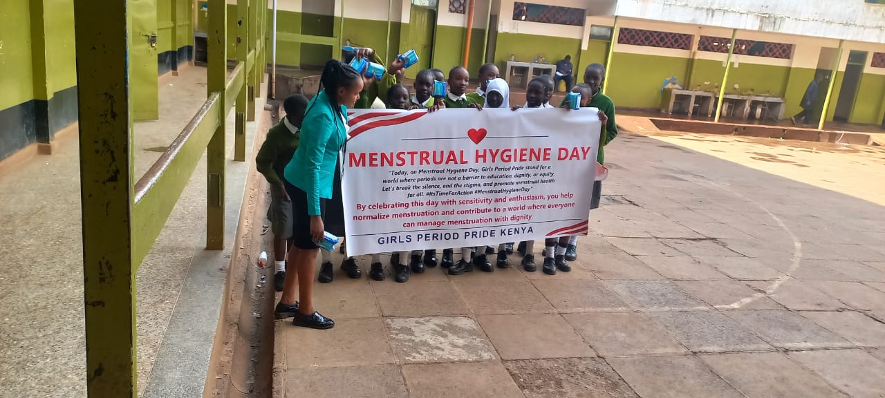 Students at Olympic Junior Secondary School holding Menstrual Hygiene Day banner with Period Pride Kenya educator, promoting awareness and breaking menstrual stigma